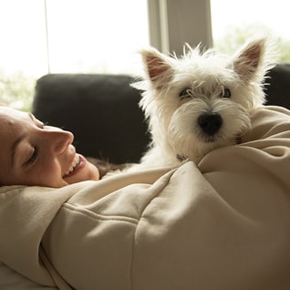 woman laying on her couch relaxing and cuddling with her Westie on her chest 